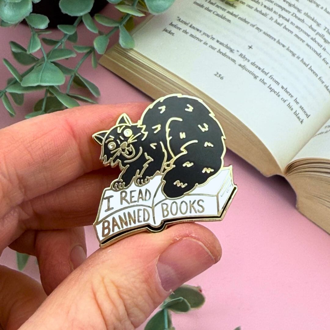 Pin with a cat design and 'I Read Banned Books' text held over an open book.