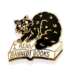 black cat hissing with arched back while standing on a open book with I REad Banned Books written on it.