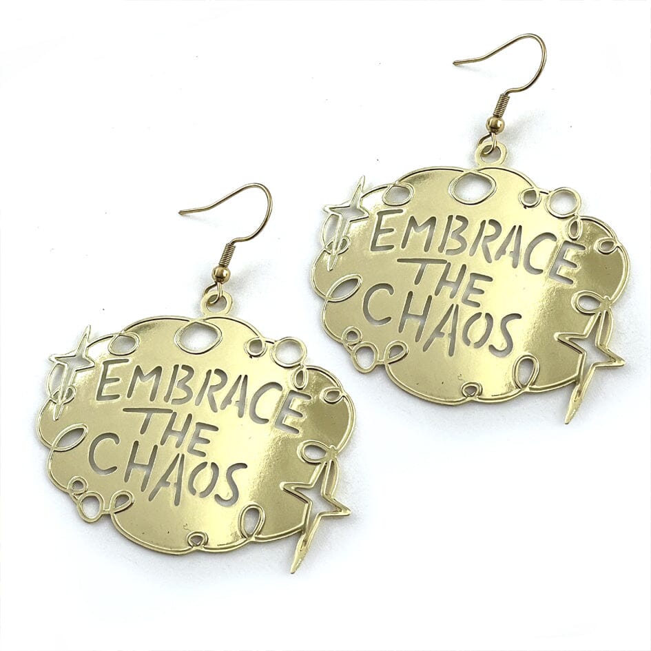 A pair of dangle brass earrings displayed on a white background. The earrings read Embrace The Chaos.