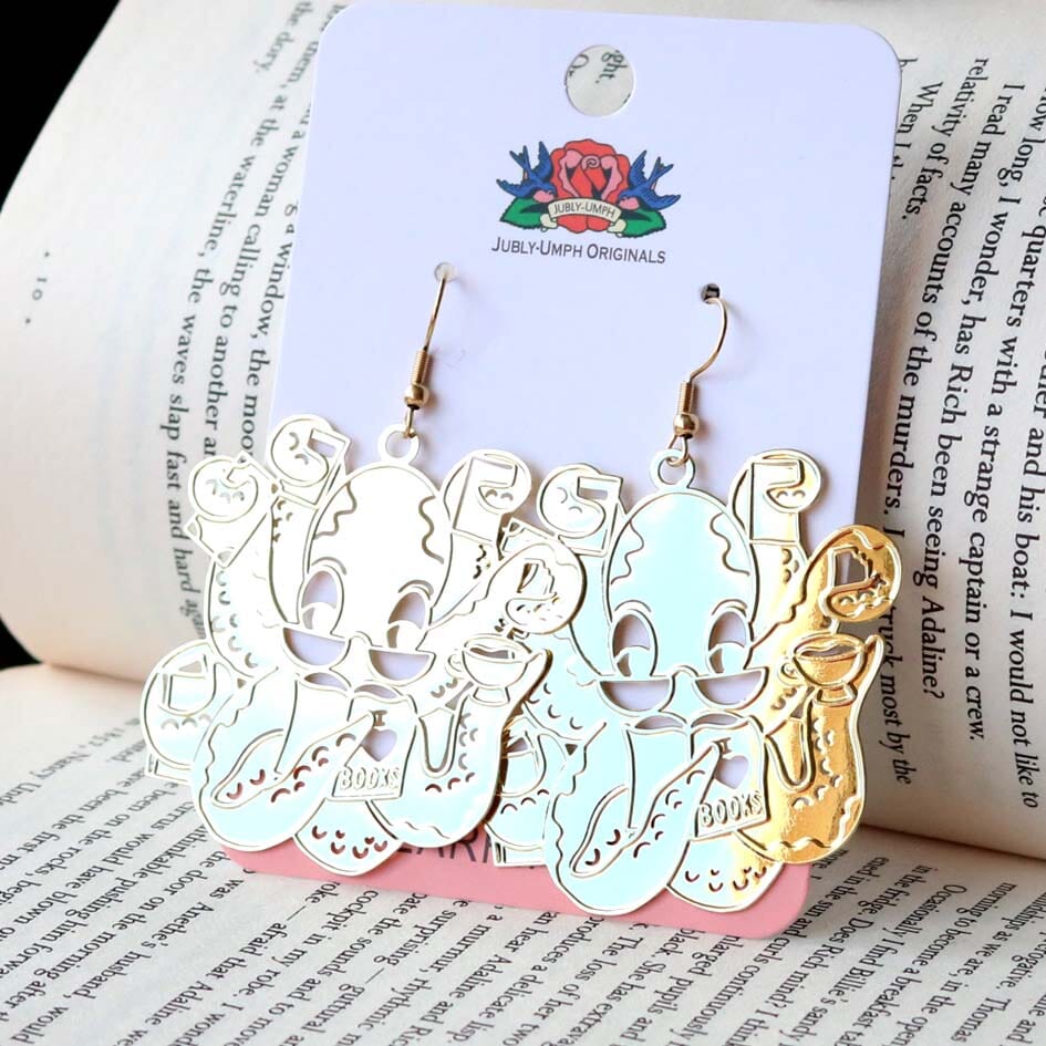 A pair of dangle brass earrings displayed on Jubly-Umph cardstock. The earrings are of an octopus wearing glasses holding books in its tentacles.