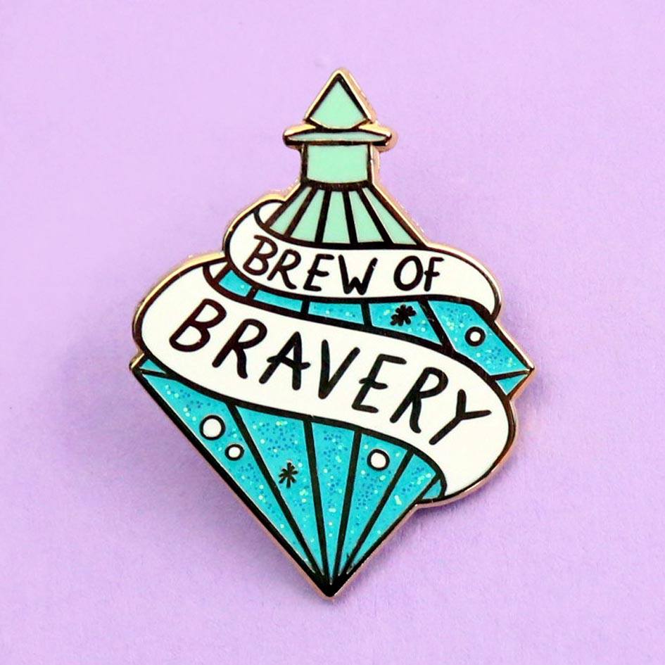 A hard enamel lapel pin on a purple background. The pin is in the profile of a diamond shaped bottle with blue glitter. The pin says Brew Of Bravery.