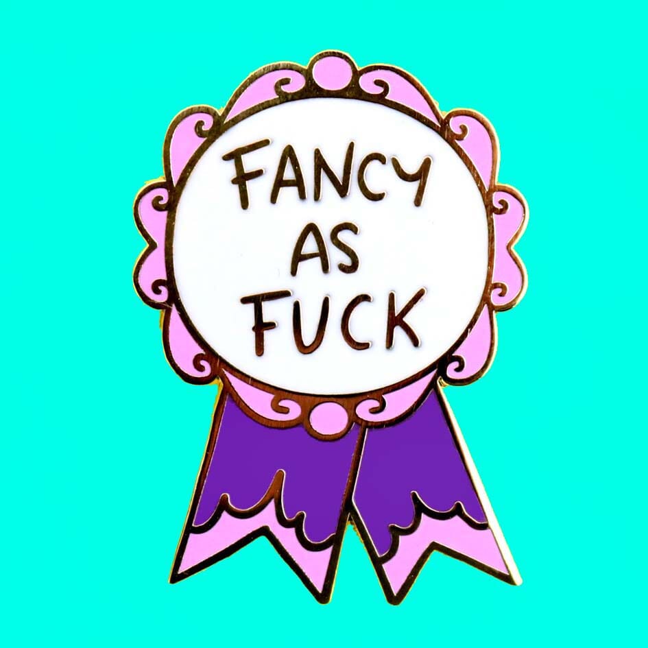 A hard enamel lapel pin on a teal background. The pin is in the shape of a pink and purple ribbon award and reads Fancy As Fuck.