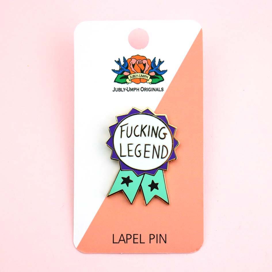 A hard enamel lapel pin being displayed on Jubly-Umph backing card. The pin is in the shape of a teal and purple ribbon award and reads Fucking Legen