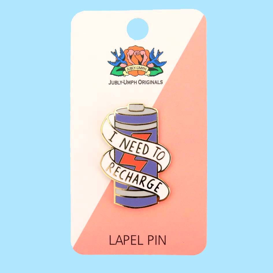 A hard enamel lapel pin displayed on a Jubly-Umph backing card. The lapel pin is in the shape of a battery and reads I Need To Recharge.
