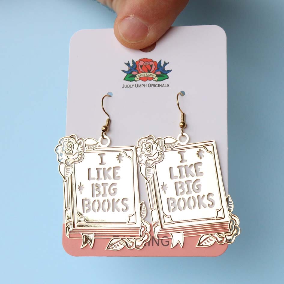 A pair of dangle brass earrings displayed on a Jubly-Umph backing card. The earrings read I Like Big Books.