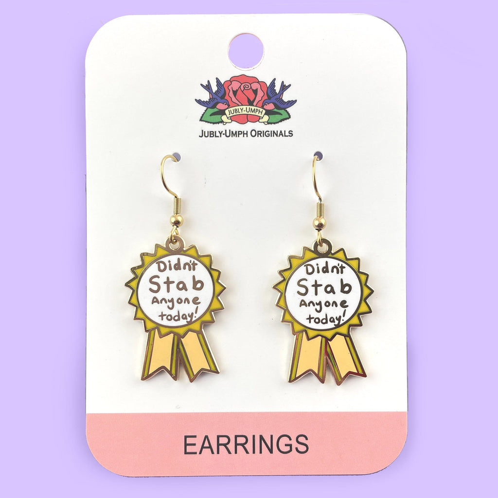 A pair of dangle earrings in the shape of an award ribbon. They are on Jubly-Umph card stock. The ribbon is yellow and white, and reads Didn’t Stab Anyone Today!