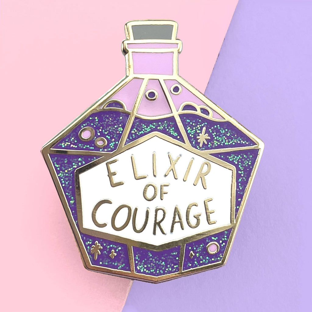 A hard enamel pin on a pink and purple background. The pin is in the shape of a bottle with purple glitter. The pin reads Elixir Of Courage.