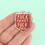 A hard enamel pin on held in the hand. The pin is in the shape of a red shield and reads Fuck Fuckity Fuck Fuck.
