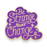 Purple and gold enamel pin with 'Be Strange Never Change' text on a white background