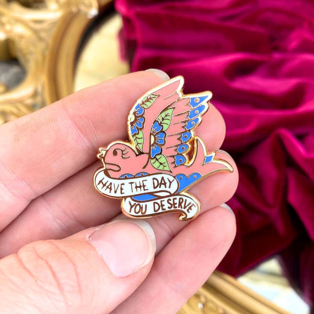 Have the Day You Deserve pin being held with mirror and velvet red background