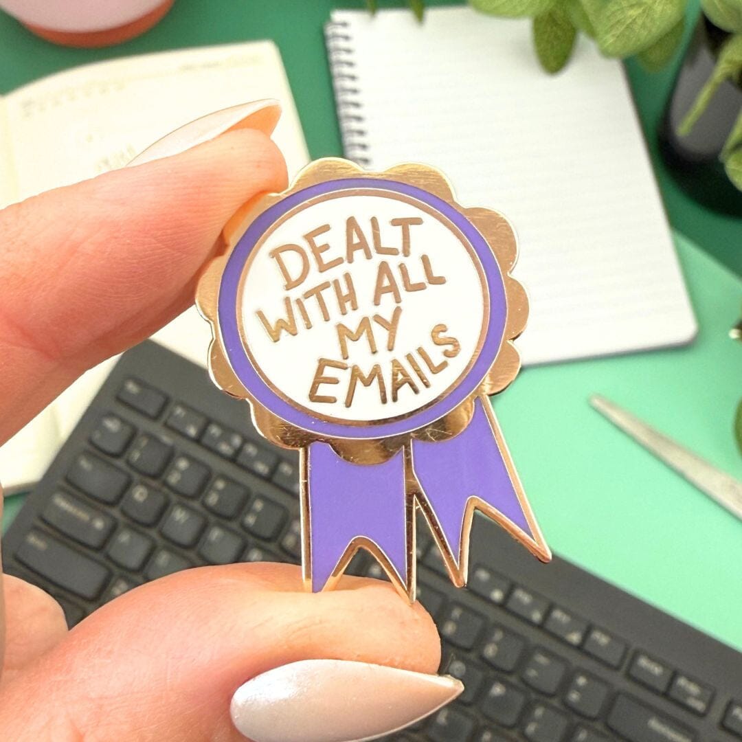 Pin with 'Dealt with all my emails' text held over a desk with office supplies.