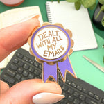 Pin with 'Dealt with all my emails' text held by a hand on a desk.