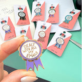 Collection of lapel pins on cards with a hand holding one pin labeled 'Dealt with all my emails'.