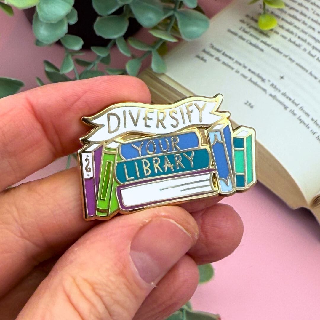 Pin with 'Diversify Your Library' text held by a hand, with an open book and plant in the background.