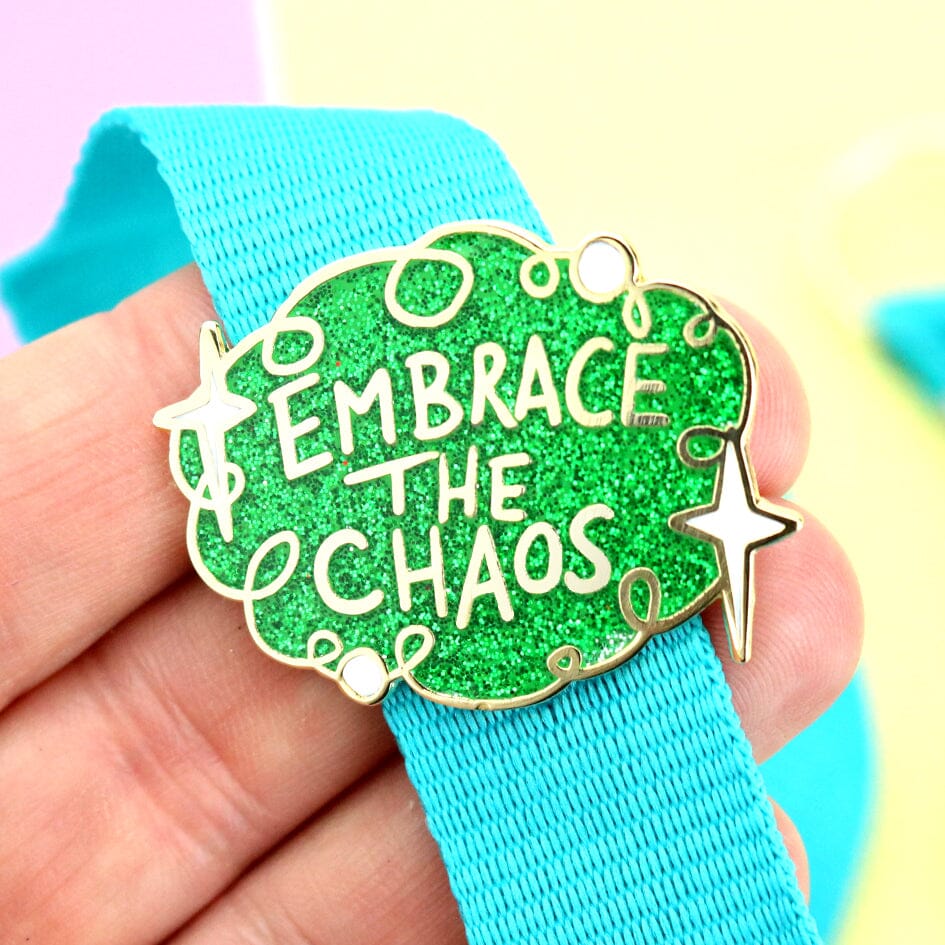A hard enamel lapel pin being held in the hand and attached to a blue lanyard. The pin is green glitter with white stars an