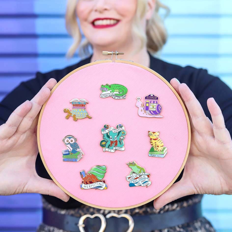 This set contains one of each design on a embroidery hoop background being held by a smiling woman: -It’s Not Hoarding If It's Books Octopus, - Bookish Snail,- There's No Such Thing As Too Many Books Frog- Books Are Purr-fect Cat- Hermiting Crab- Audiobook Lover Owl- Slow and Steady Reader Tortoise- So Many Books So Little Time Crocodile. 
