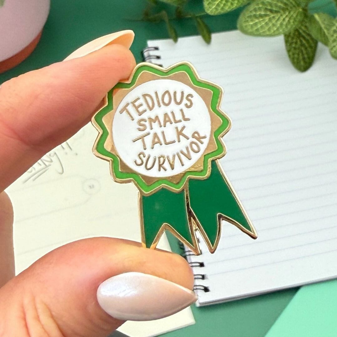 Pin with 'Tedious Small Talk Survivor' text held by a hand against a green background