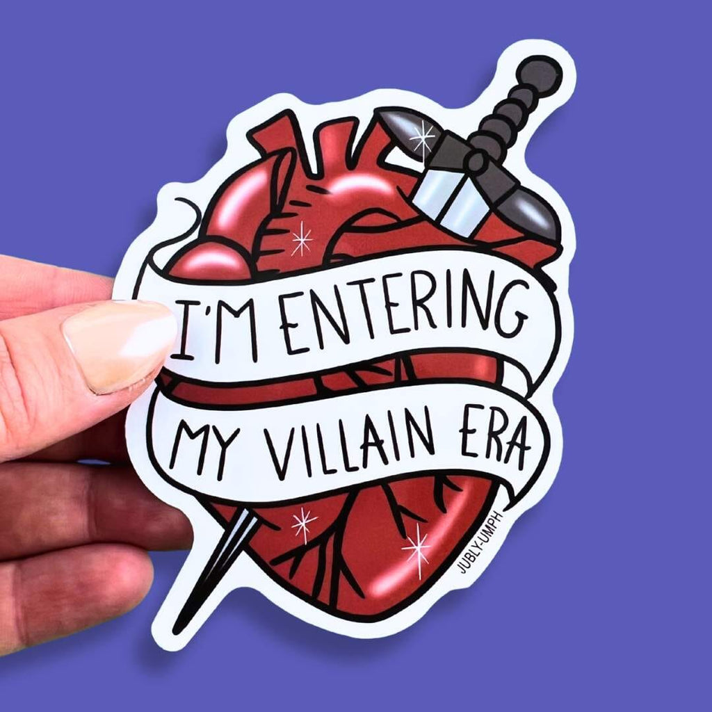 The vinyl sticker is in the shape of a human heart with a dagger held in the hand against a purple background. The sticker reads I'm Entering My Villain Era.