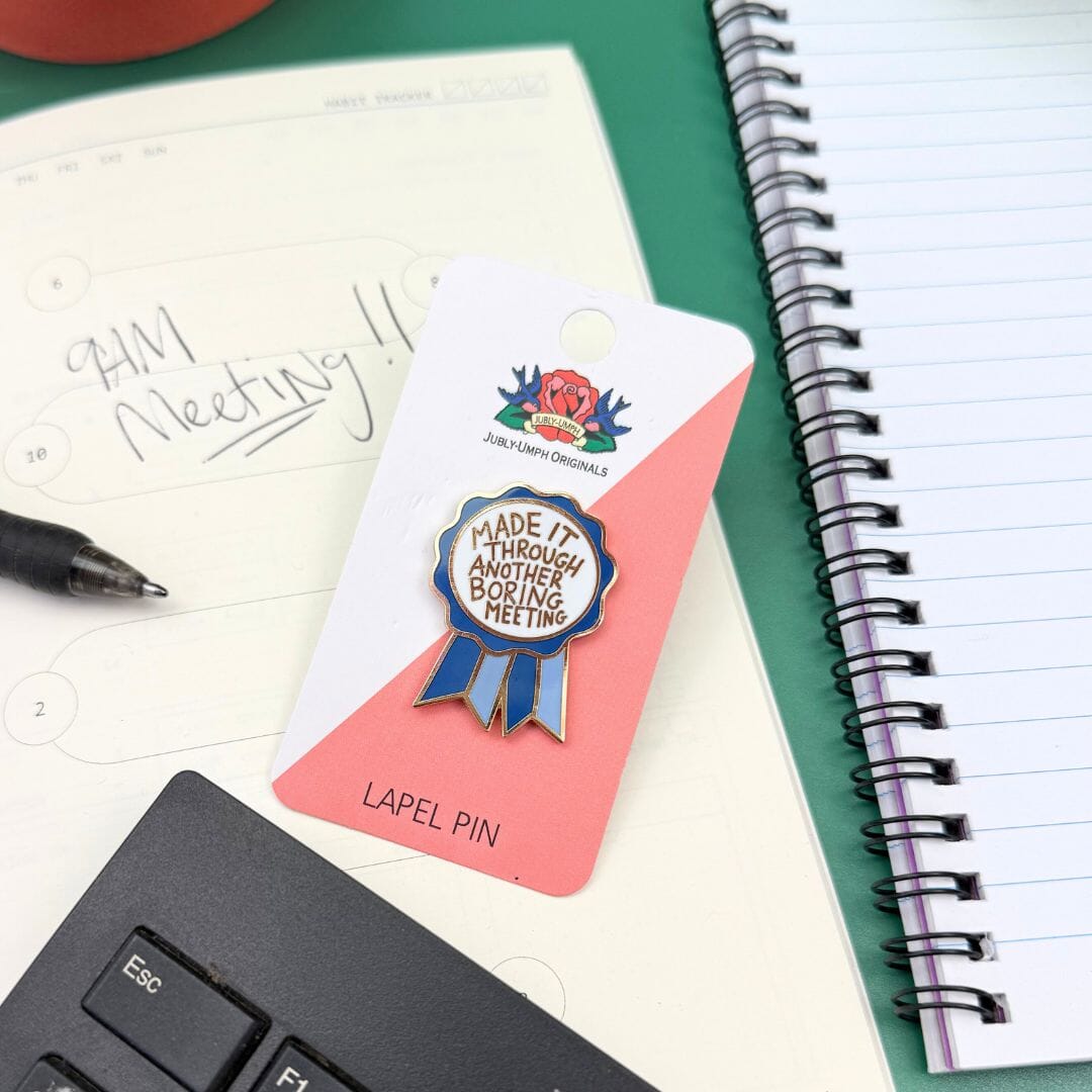 Lapel pin on a card with a notebook, pen, and keyboard in the background