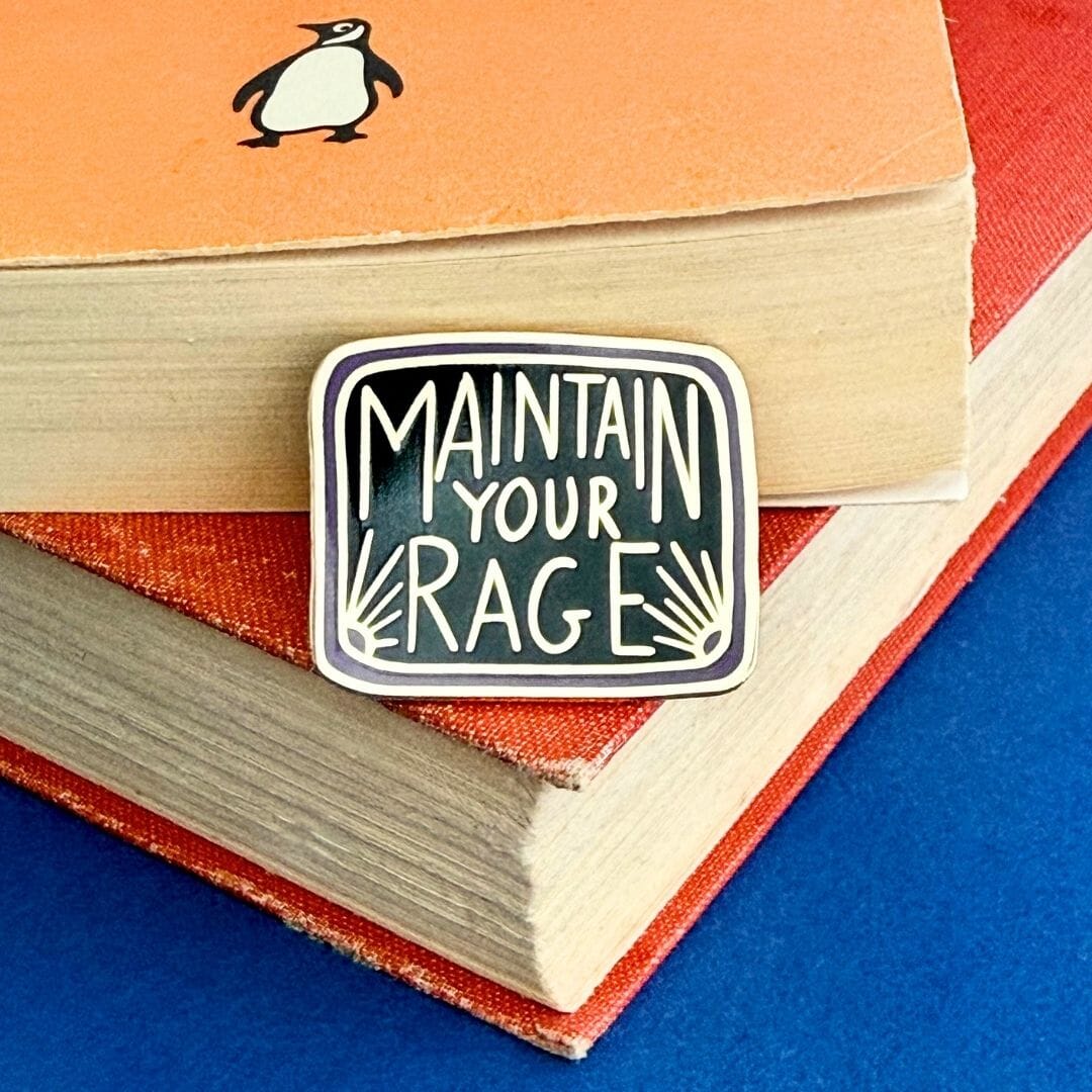 Enamel pin with 'Maintain Your Rage' text on a book