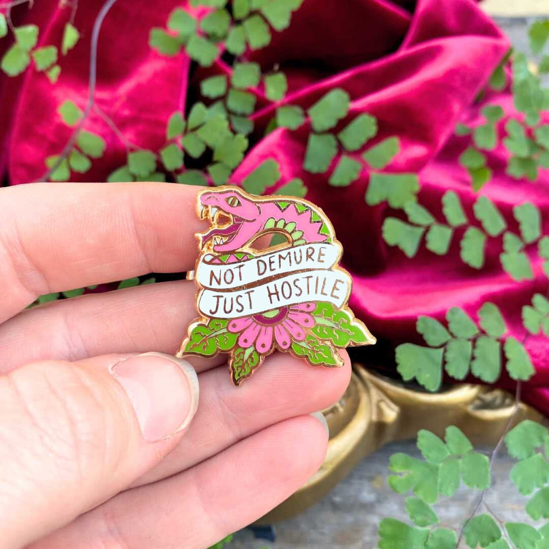 Not Demure just hostile pin being held with plant and velvet red background