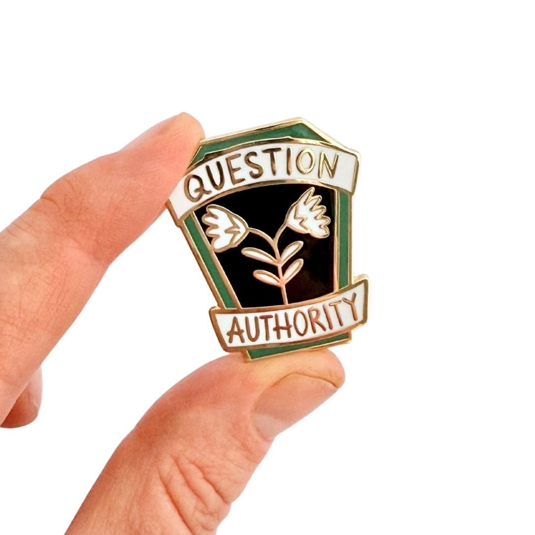 Pin with 'Question Authority' text held by a hand on a white background