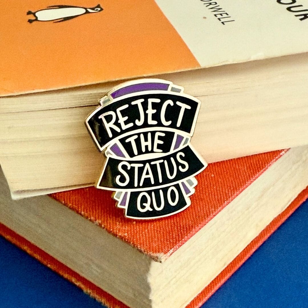 Pin with 'Reject the Status Quo' text on a stack of books
