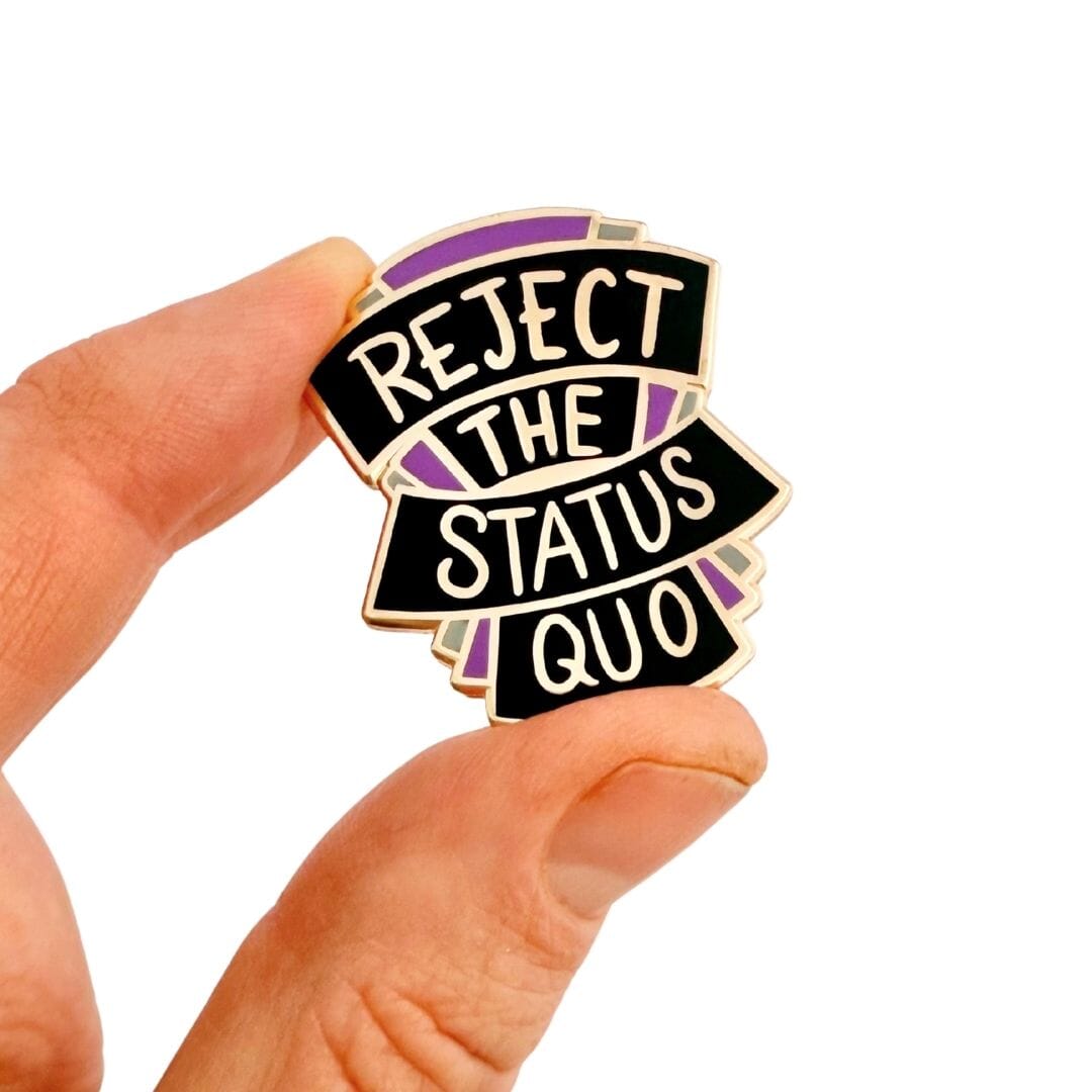 Pin with 'Reject the Status Quo' text held by a hand on a white background