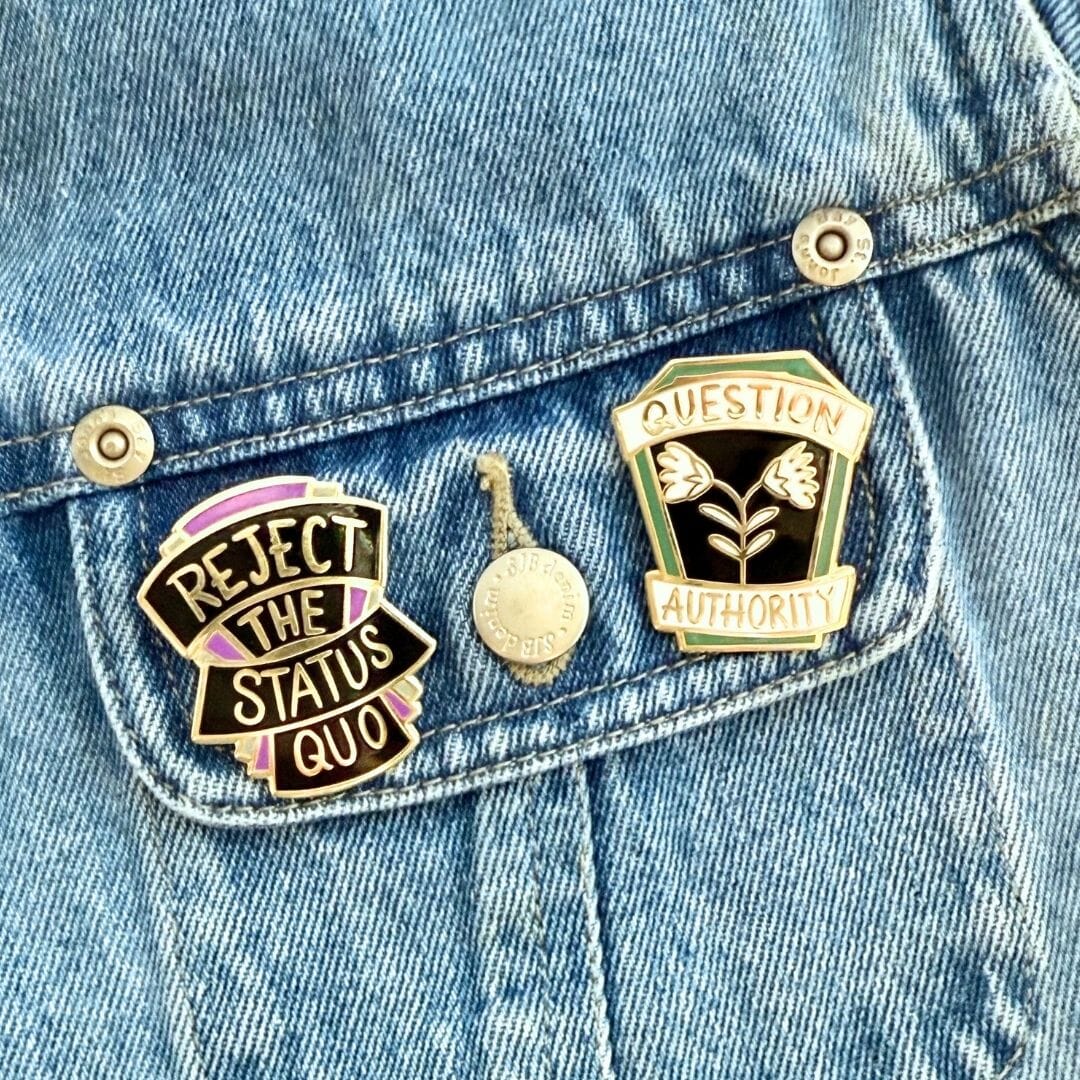 Two pins on a denim jacket, one with 'Reject the Status Quo' and the other with 'Question Authority'.