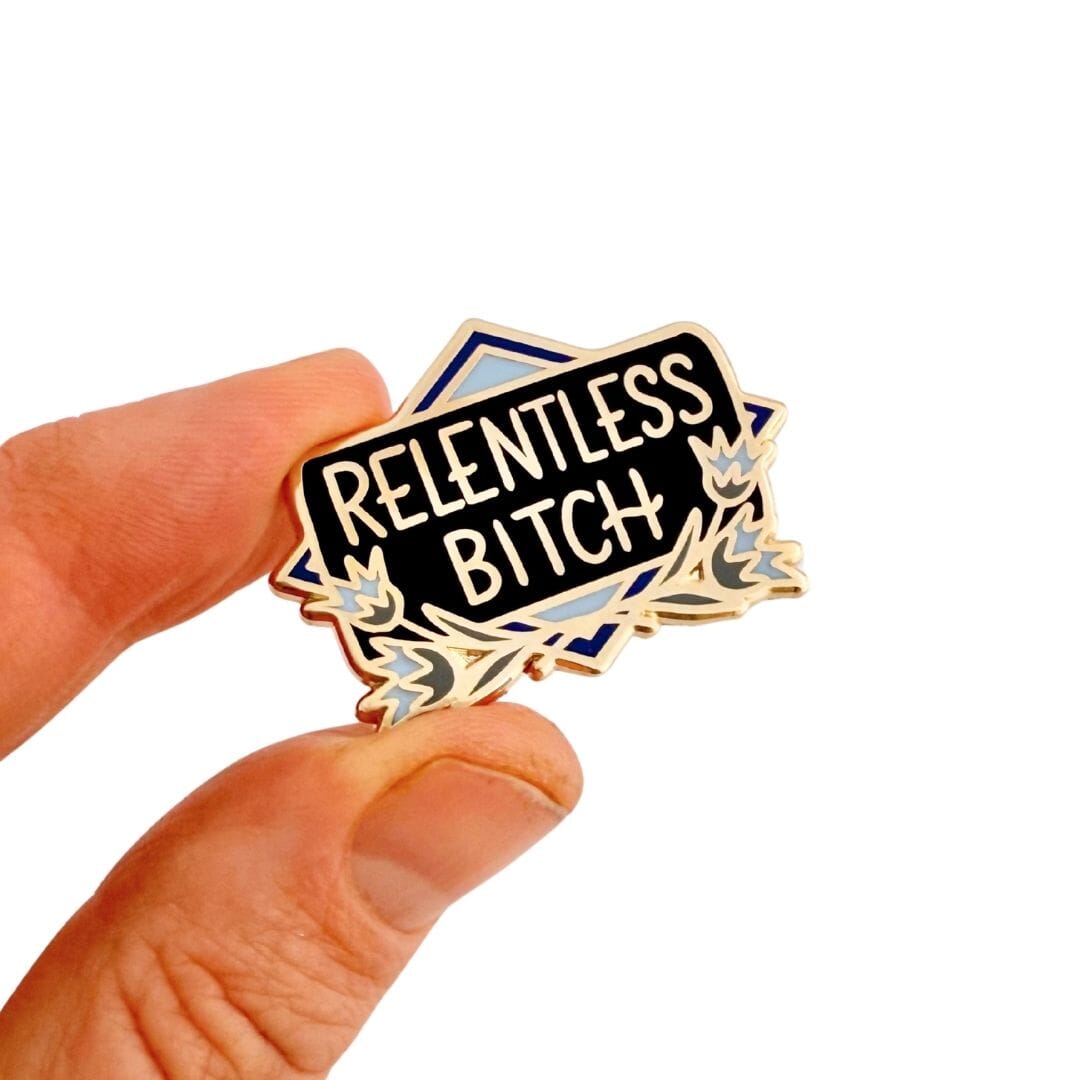 Pin with 'RELENTLESS BITCH' text held by a hand on a white background
