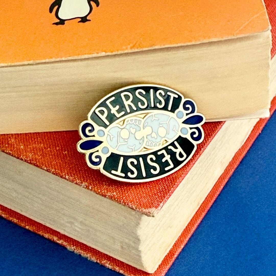 Enamel pin with 'Persist Resist' design on a book
