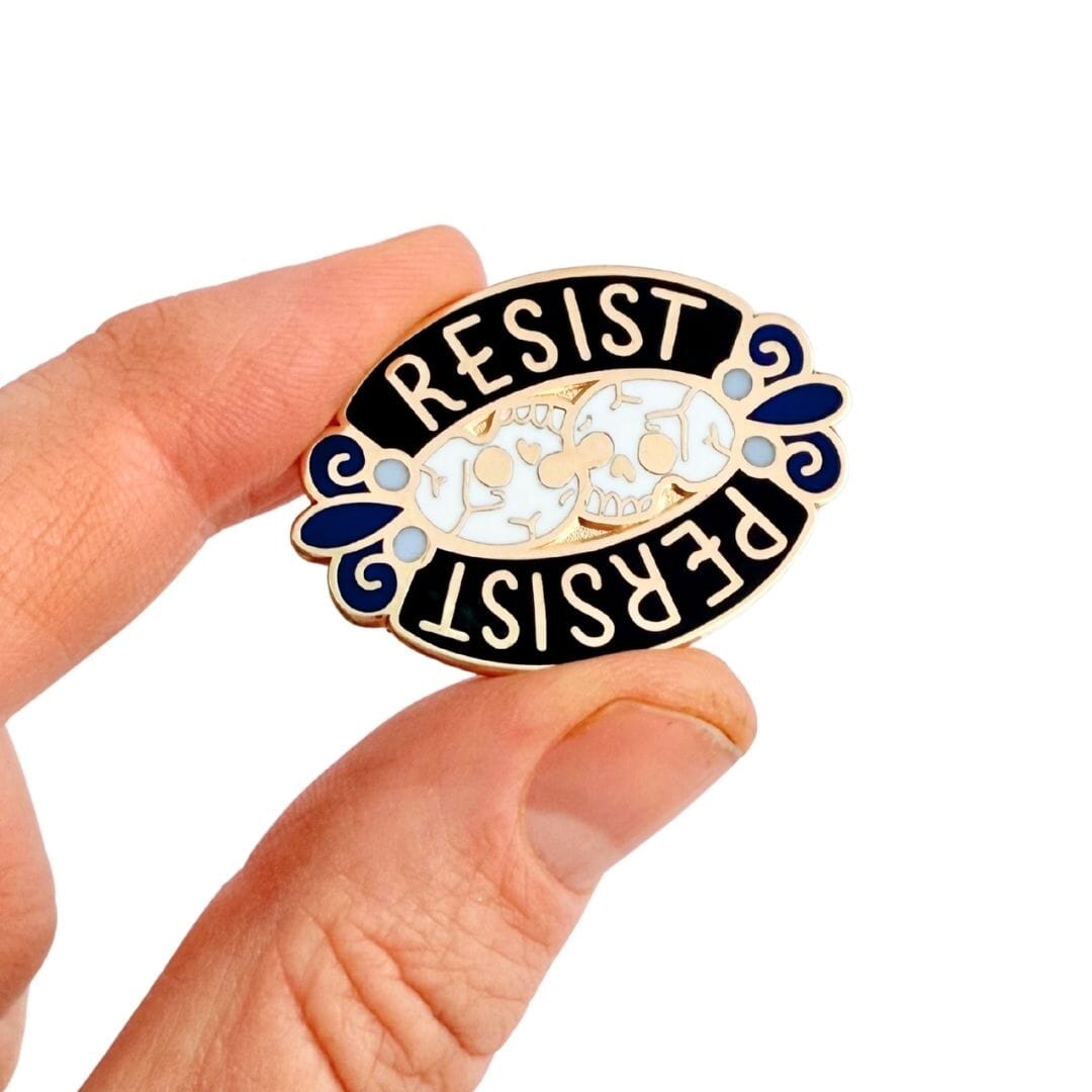 Pin with 'RESIST' and 'PERSIST' text held by a hand on a white background
