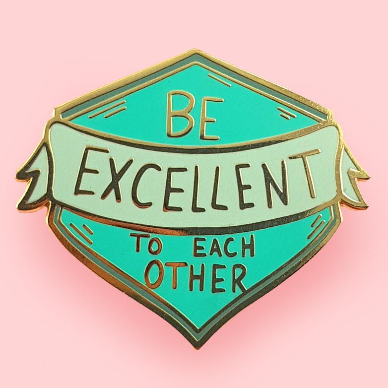 Enamel pin in a shield shape with a banner draped on it. The text reads "Be Excellent to each other". The pin colour is mint and sea green