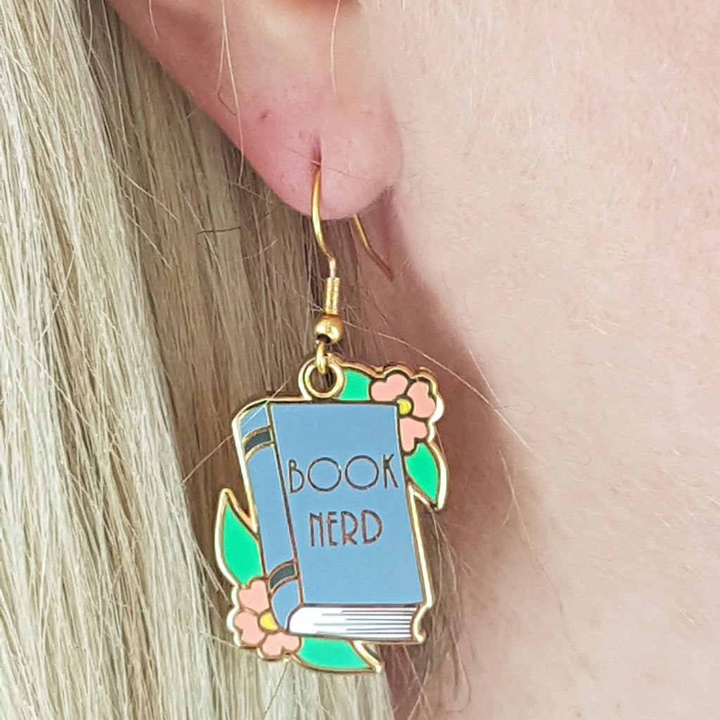 A single earring displayed from an ear lobe. The earring says Book Nerd in the middle of a blue book.