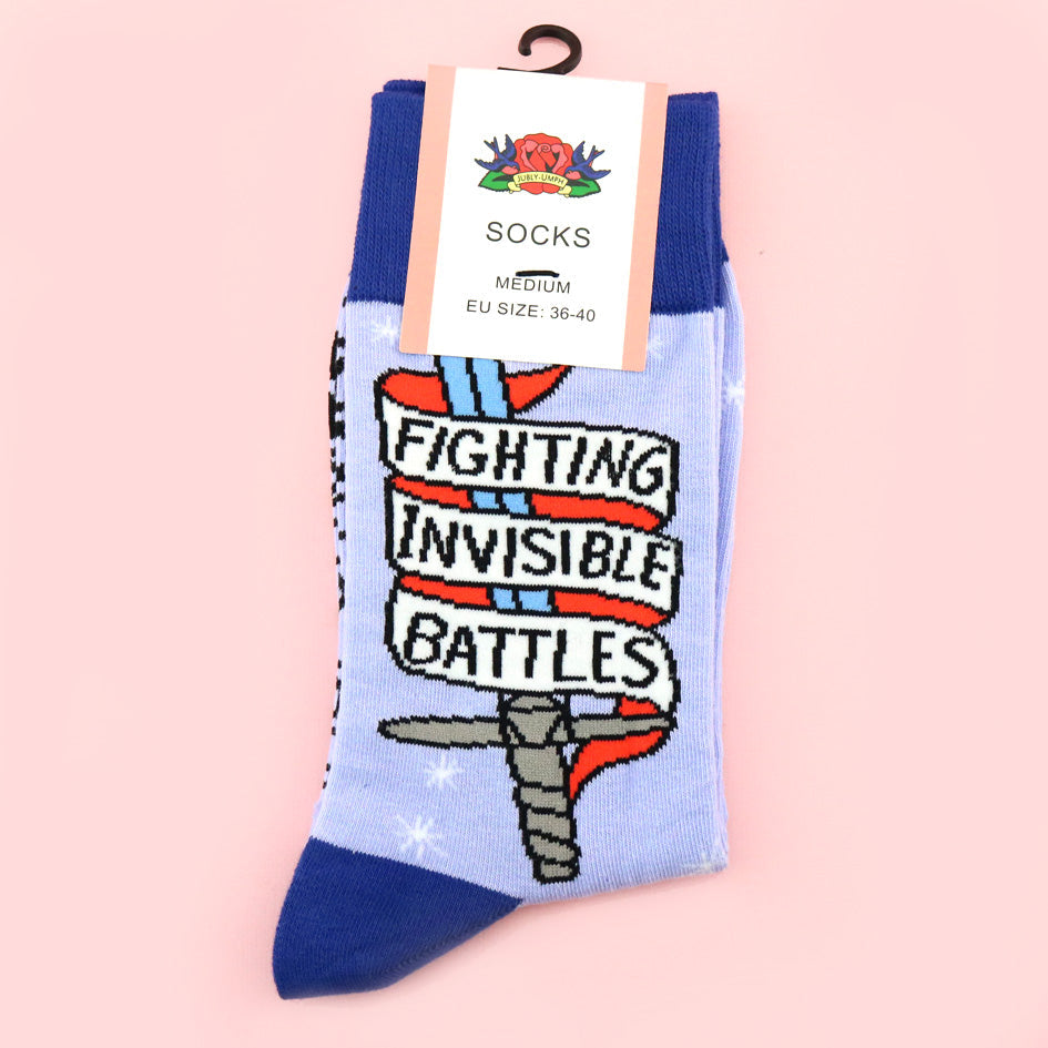 A pair of socks standing against a pink background. The socks are blue and read Fighting Invisible Battles inside a dagger.