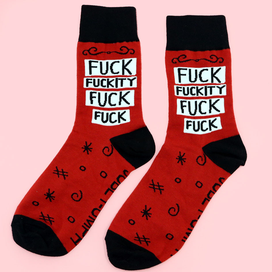 A pair of socks standing against a pink background. The socks are red and black and read Fuck Fuckity Fuck Fuck.