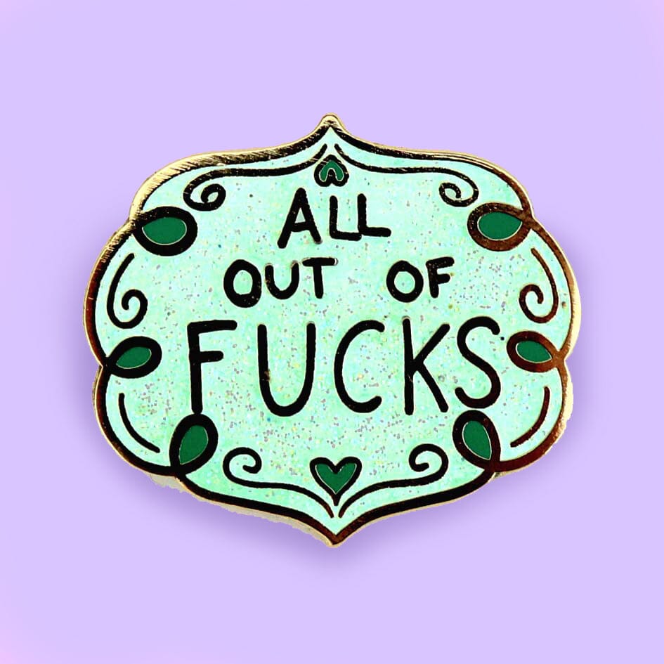 A hard enamel lapel pin against a purple background. The pin has blue sparkly enamel and reads All Out Of Fucks.