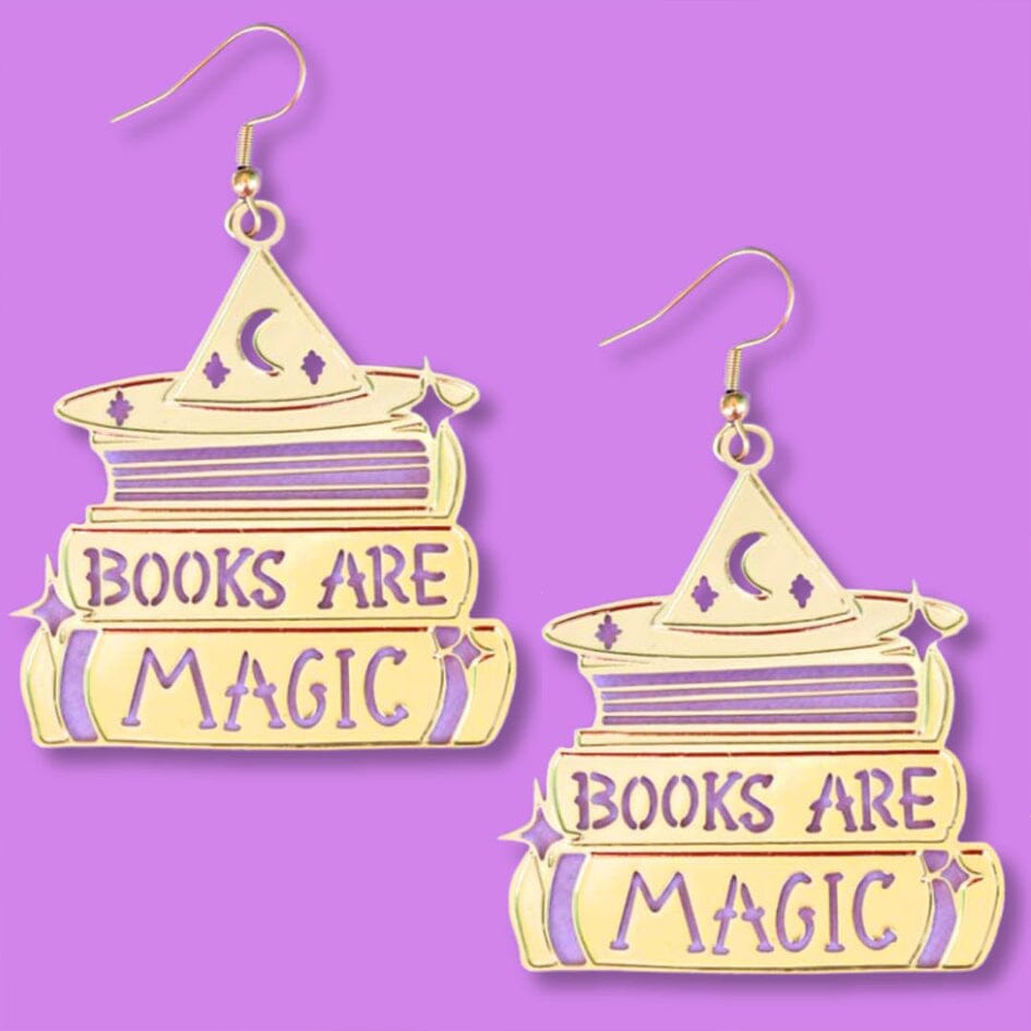A pair of dangle brass earrings displayed on a purple background. The earrings say Books are Magic with books and a witch’s hat.  