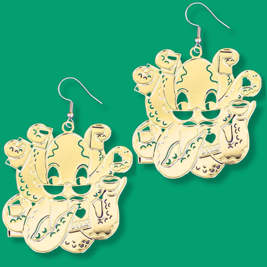 A pair of dangle brass earrings displayed on a green background. The earrings are of an octopus wearing glasses holding books in its tentacles.