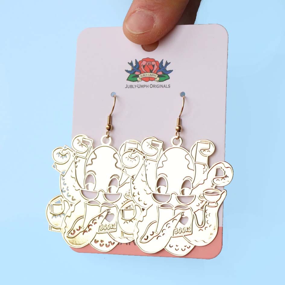 A pair of dangle brass earrings displayed on Jubly-Umph cardstock. The earrings are of an octopus wearing glasses holding books in its tentacles.