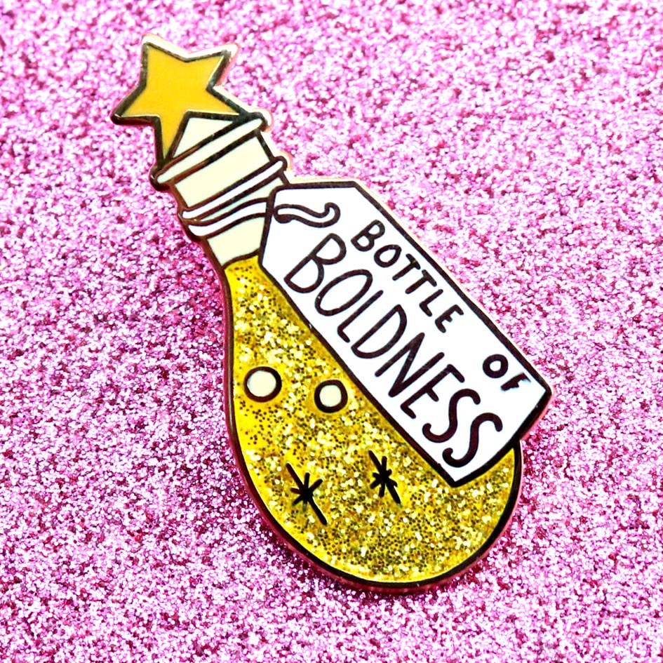 A hard enamel lapel pin displayed on pink glitter background. The pin is in the profile of a bottle with yellow glitter. The pin says Bottle of Boldness.