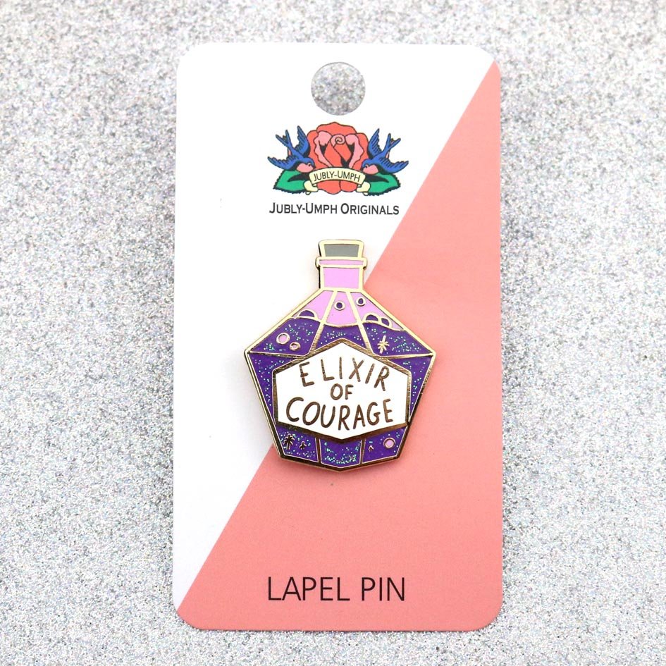 A hard enamel pin on Jubly-Umph cardstock. The pin is in the shape of a bottle with purple glitter. The pin reads Elixir Of Courage.