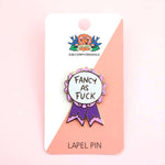 A hard enamel lapel pin on a Jubly-Umph backing card. The pin is in the shape of a pink and purple ribbon award and reads Fancy As Fuck.