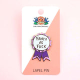 A hard enamel lapel pin on a Jubly-Umph backing card. The pin is in the shape of a pink and purple ribbon award and reads Fancy As Fuck.