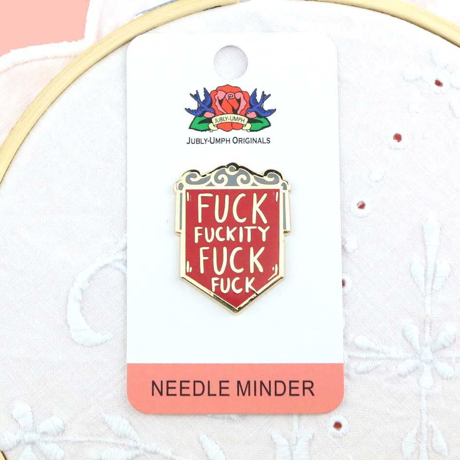 A hard enamel magnetic needle minder on Jubly-Umph backing card. The pin is in the shape of a red shield and reads Fuck Fuckity Fuck Fuck.