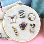 Hard enamel lapel pins displayed on a embroidery hoop. The pin is in the shape of a seam ripper. The lapel pin reads I Can Fix It. The other pins read MakeDo Mend, Stitching Is My Therapy, Let's Get Stabby, Keep Calm and Sew On and Mischief Maker.