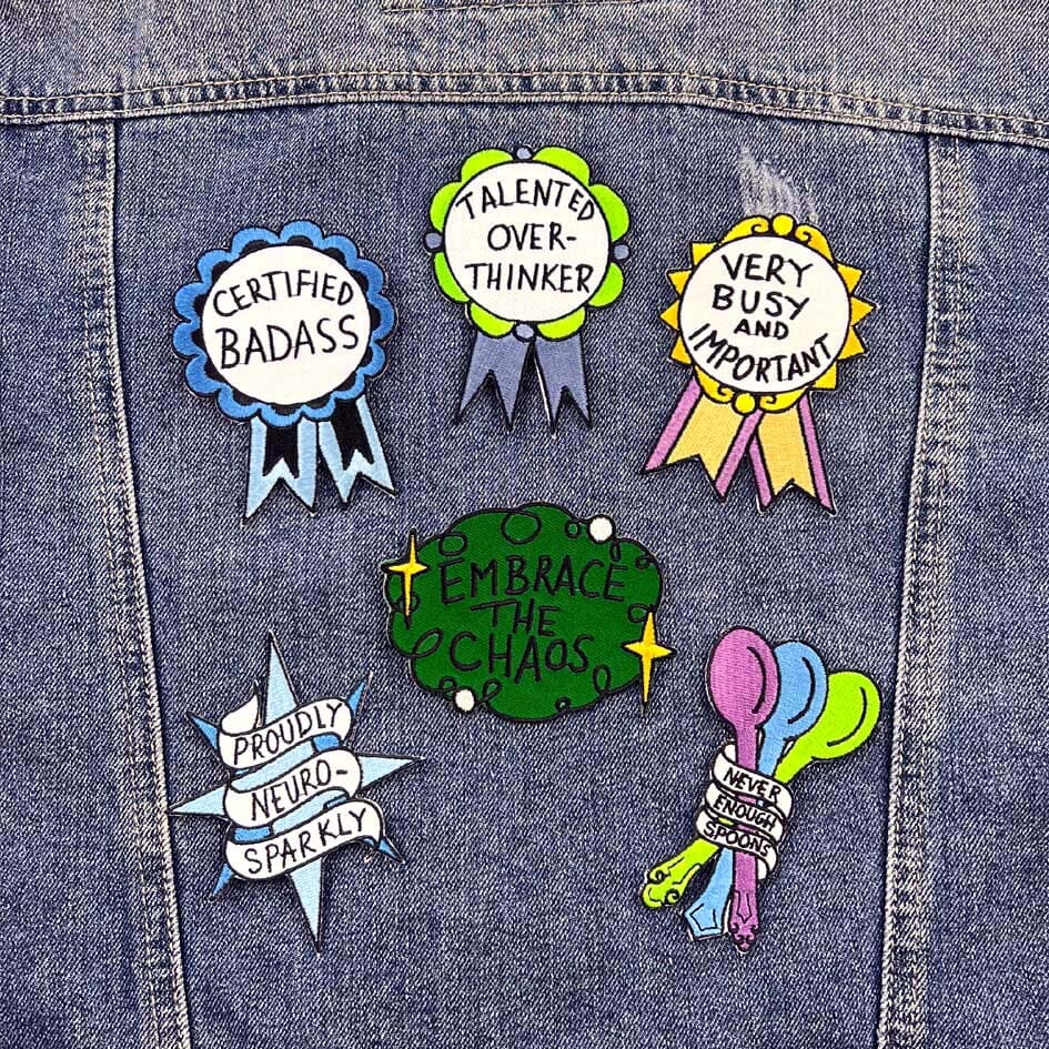 Six iron on embroidered patches sit on a denim jacket. They read Certified Badass, Talented Overthinker, Very Busy and Important, Proudly Neuro-Sparkly, Embrace the Chaos and Never Enough Spoons.