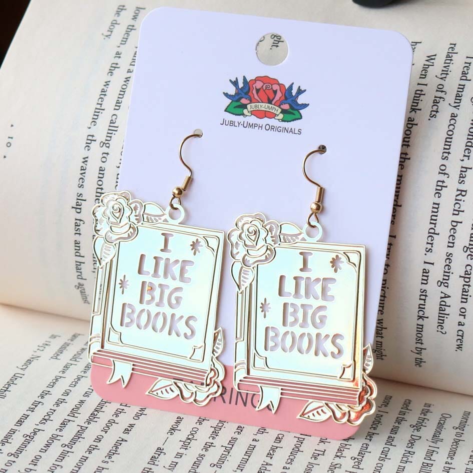 A pair of dangle brass earrings displayed on a Jubly-Umph backing card. The earrings read I Like Big Books.