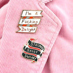Hard enamel lapel pins on a pink jacket. The first lapel pin reads I'm A Fucking Delight. The second reads Strong Sassy Sweary.