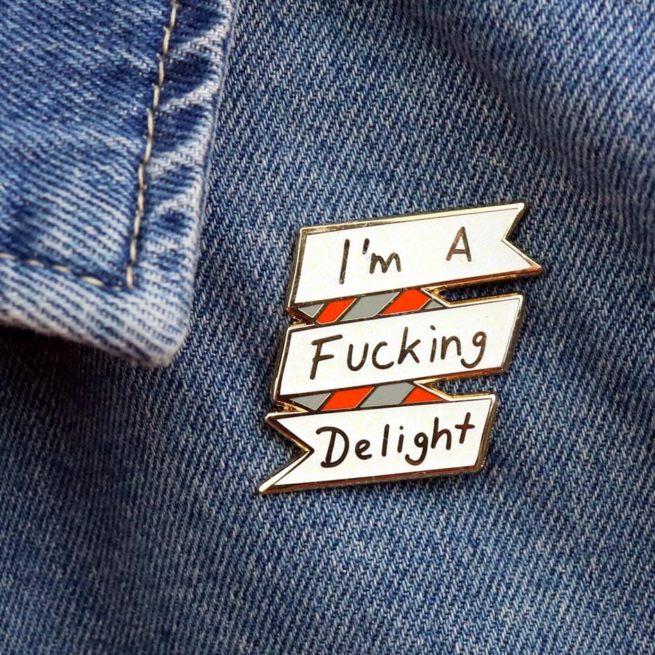 A hard enamel lapel pin being displayed on a denim jacket. The lapel pin reads I'm A Fucking Delight.